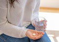 Person holds a glass of water with a round white tablet in hand