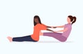 Female personal trainer doing stretching exercises with african american girl fitness instructor helping woman to Royalty Free Stock Photo