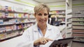 Female pharmacist reading emails off digital tablet while assistant organises medicines