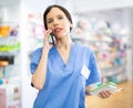 Female pharmacist talking on mobile phone and taking notes in a notebook in pharmacy Royalty Free Stock Photo