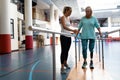 Female physiotherapist helping disabled senior woman walk with parallel bars in sports center Royalty Free Stock Photo