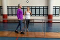 Female physiotherapist helping disabled senior woman walk with parallel bars in sports center Royalty Free Stock Photo
