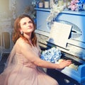 A female pianist sits at a retro piano with a bouquet of blue flowers