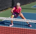 Female pickelball player leans low and volleys the ball over the net
