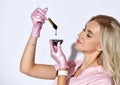 Female in pink scrubs and disposable gloves is posing isolated on white. Holding brush, glass bowl with black liquid. Close up Royalty Free Stock Photo