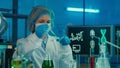 A female pipettes a green liquid into a glass test tube. A woman in a white medical gown, bonnet, blue gloves and a mask Royalty Free Stock Photo