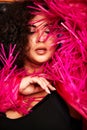 Female Plus size model posing in the studio, front face portrait, in rose feathers. The woman is looking with sensuality