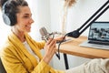 Female podcaster recording her podcast using microphone and laptop at his small home broadcast studio
