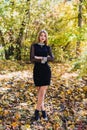 Female porteait in autumn park. Beaurtiful woman in black dress posing with yellow trees