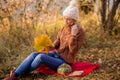 Female portrait. Lonely beautiful blonde in a white knitted hat, brown sweater sits on a plaid in the park, holds a bouquet of