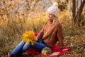 Female portrait. Lonely beautiful blonde in a white knitted hat, brown sweater sits on a plaid in the park, holds a bouquet of