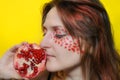 Female portrait with make-up on her face. Young woman with garnet. Girl and half of pomegranate on a yellow background Royalty Free Stock Photo