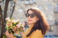 Female portrait of sensual brunette woman in dark sunglasses and yellow jacket holding a big bouquet of colorful flowers Royalty Free Stock Photo