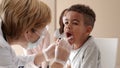 Female practitioner doctor in white coat protective face mask make medical general health exam, larynx check up of infant african