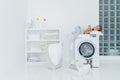 Female preschooler sleeps on washing machine, being tired with washing, poses in white big laundry room with basket and basin full