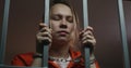 Female prisoner holds metal bars, stands in jail cell in handcuffs