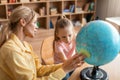 Female private preschool teacher teaching smart girl about globe, having home class, sitting at desk in living room Royalty Free Stock Photo