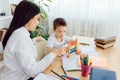 Female private tutor helping young student with homework at desk in bright child`s room