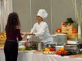 Female professional chef prepares the pasta dish at the buffet for the customer