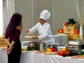 Female professional chef prepares the pasta dish at the buffet for the customer