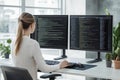A female programmer works intently at a computer desk, utilizing dual monitors that display intricate lines of code in a