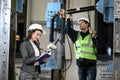 Female project manager in a business suit and white hard hat holds laptop and discusses product details with the chief engineer