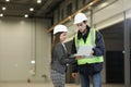 Female project manager in a business suit and white hard hat holds laptop and discusses product details with the chief engineer