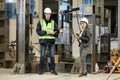 Female project manager in a business suit and white hard hat holds laptop and discusses product details with the chief engineer