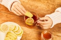 Female putting a ginger slice into the cup of hot tea with honey and lemon - home treatment