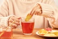 Female putting a ginger slice into the cup of hot tea with honey and lemon - home treatment