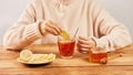 Female putting a ginger slice into the cup of hot tea with honey and lemon - home treatment