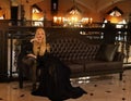 A female queen, blonde in a black dress, sits on a wooden throne Royalty Free Stock Photo