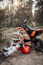 Female racer wearing motocross outfit with semi naked torso sitting on sand next to her bike in the forest Royalty Free Stock Photo