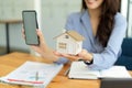 Female real estate agent showing house model and picture in smartphone Royalty Free Stock Photo