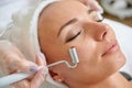 Female receiving electric facial treatment by cosmetologist wearing gloves professional services
