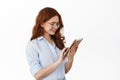 Female redhead office manager working on tablet, reading book on device, wearing glasses, working with gadget, standing Royalty Free Stock Photo