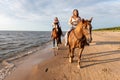 Female riders galloping along a sandy beach, with the sun glinting off of the ocean Royalty Free Stock Photo