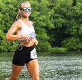 Female runner carrying cell phone smiling passing lake during 10K race