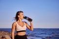 Female runner drinks water from bottle during running near coast.