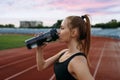 Female runner drinks water, training on stadium