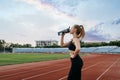 Female runner drinks water, training on stadium