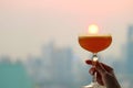 Female`s hand holding a cocktail glass against setting sun with blurry skyscrapers in backdrop Royalty Free Stock Photo