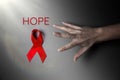 A female`s hand reaches for the red ribbon. The dark background with the light. The inscription hope. The concept of world AIDS