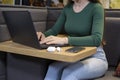 Female`s hands with cell phone in front of laptop computer, sits at cafeteria, surrounded with mug of coffee and modern laptop Royalty Free Stock Photo