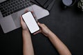 A female`s hands holding a smartphone mockup over modern black office desk with laptop Royalty Free Stock Photo