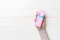 Female`s hands holding striped gift box with colored ribbon on white rustic wooden background. Christmas concept or other holiday Royalty Free Stock Photo