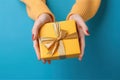 Female\'s hands in yellow and light blue, cyan tone, holding a gift box on yellow pastel background. Christmas and Valentine\'s Da