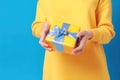 Female\'s hands in yellow and light blue, cyan tone, holding a gift box on yellow pastel background. Christmas and Valentine\'s Da