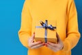 Female\'s hands in yellow and light blue, cyan tone, holding a gift box on yellow pastel background. Christmas and Valentine\'s Da