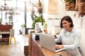 Female Sales Assistant Working On Laptop Behind Sales Desk Of Florists Store